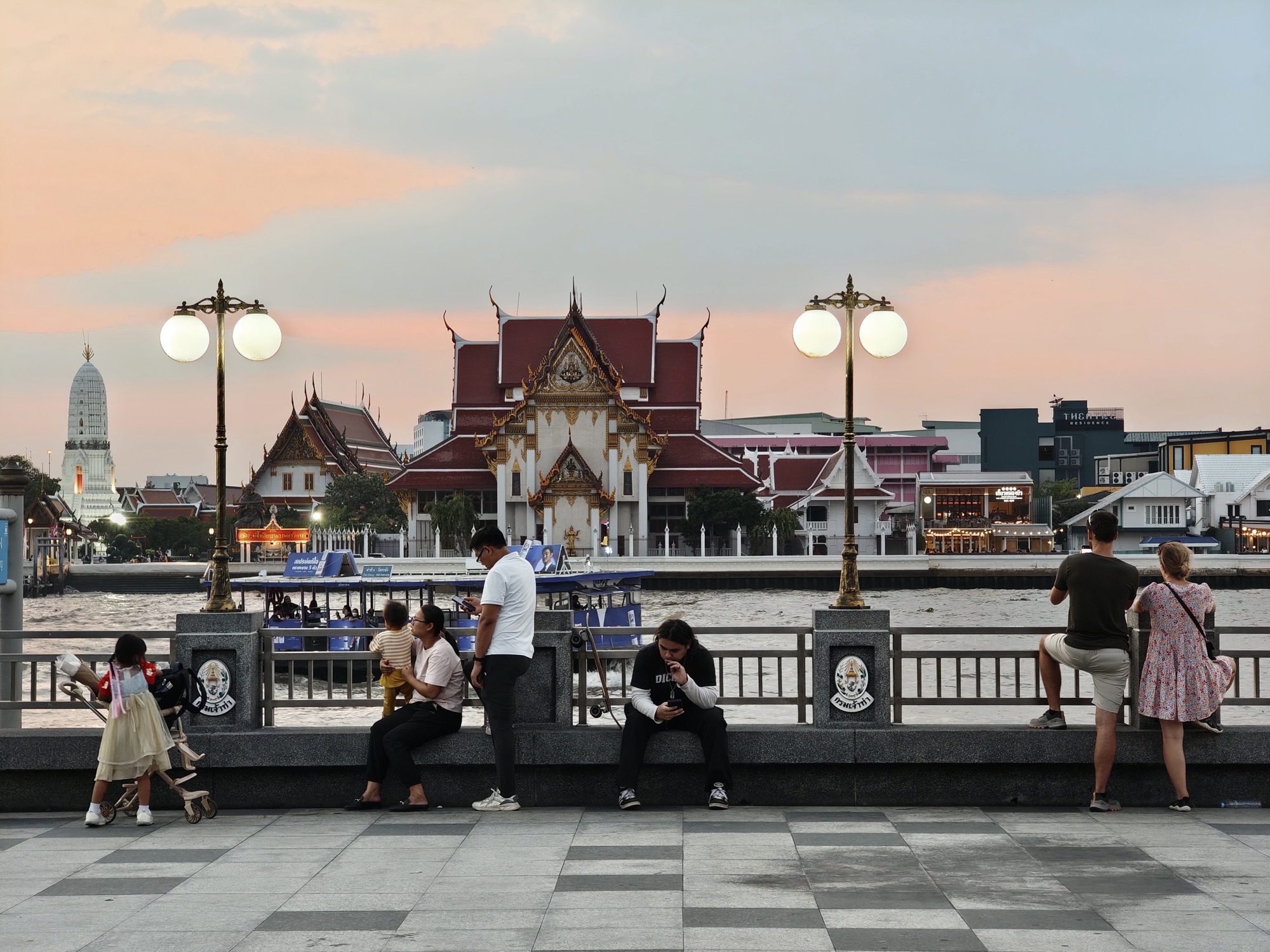 Families relaxing on the Chao Phraya riverfront promenade at golden hour in Bangkok