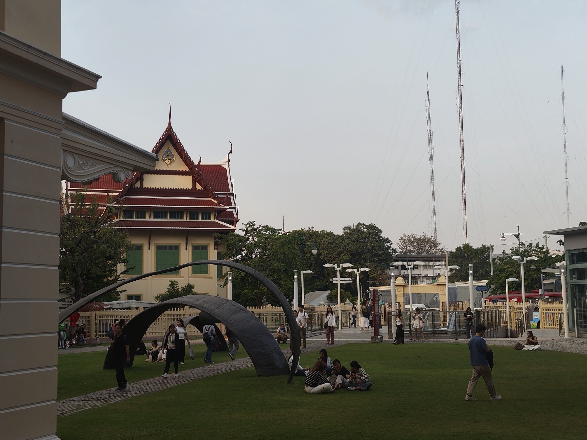 Families and children on a lawn in an open public space in Bangkok's old town, a heritage building behind them