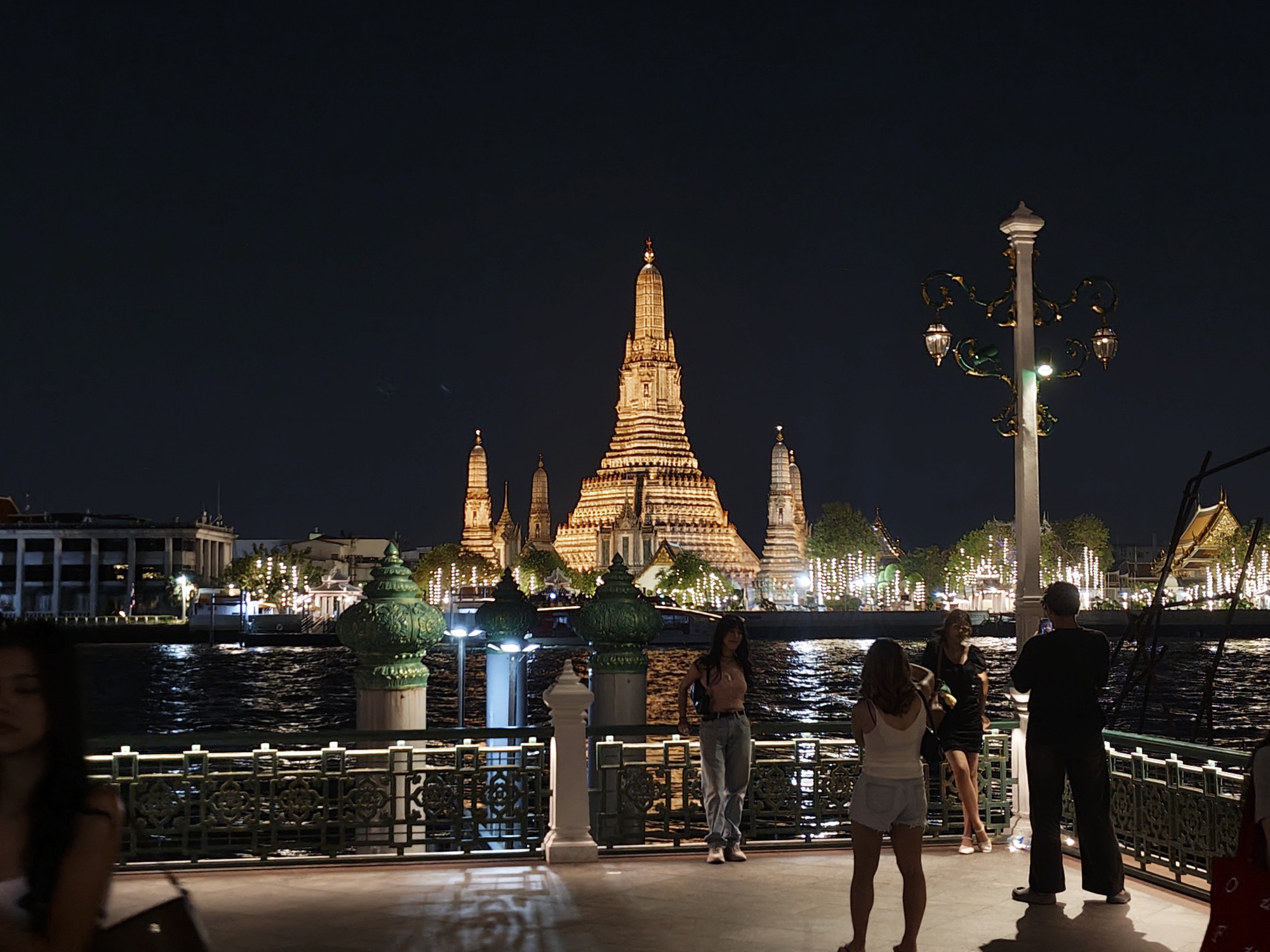 People hanging out on a Bangkok street corner at night, old shophouses lit under traffic signals